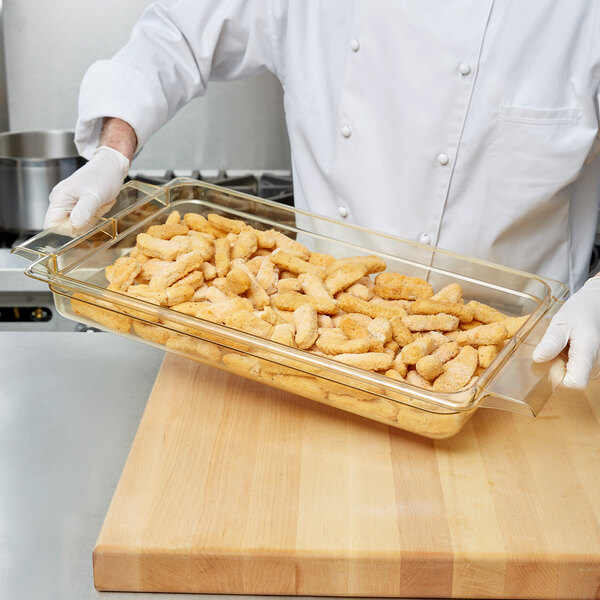 A person in a white coat holding a Cambro amber plastic food pan of chicken nuggets.