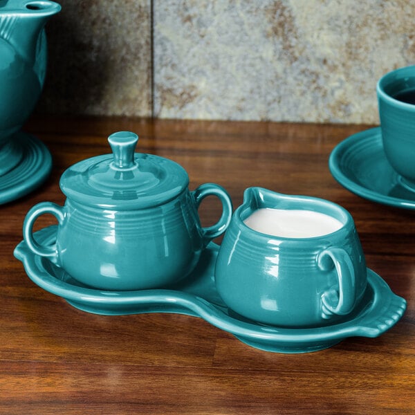 A turquoise Fiesta cream and sugar tray with cups and dishes on a white surface.