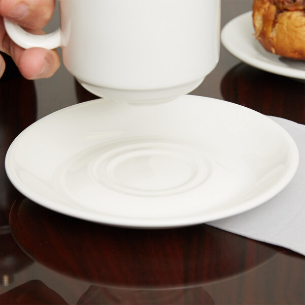 A hand pouring coffee into a white Arcoroc saucer with a white Arcoroc cup on it.