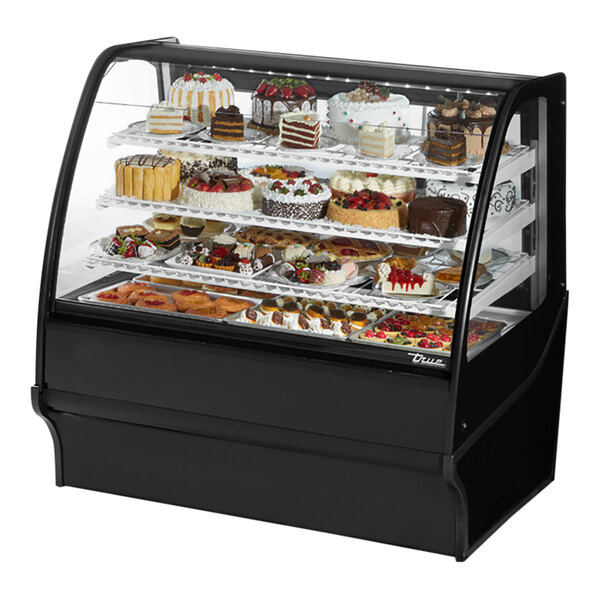 A True black refrigerated curved glass bakery display case filled with cakes including a cake with strawberries and a cake with red flowers.