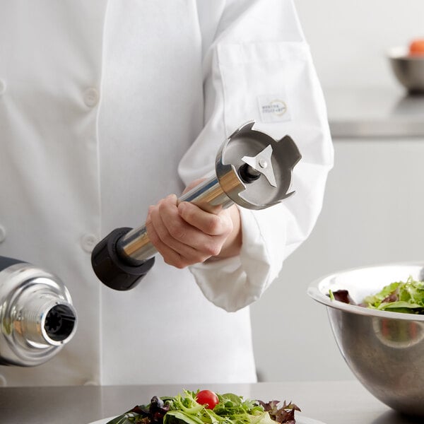 A person in a white coat using an AvaMix heavy-duty blending shaft to blend a salad.