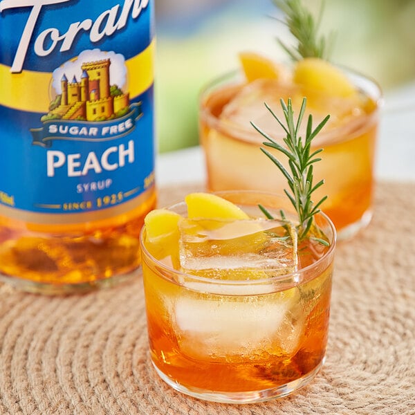 A glass of Torani sugar-free peach flavoring with ice and a rosemary sprig.
