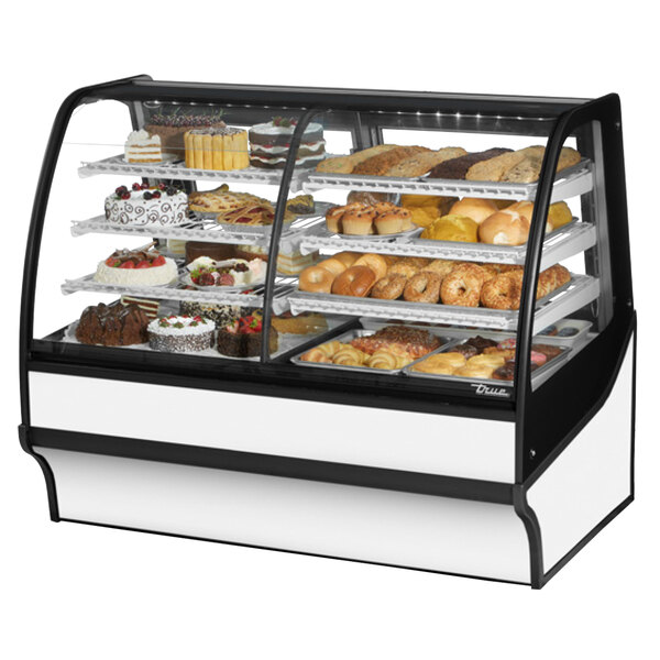 A True curved glass white dual service refrigerated bakery display case on a counter with different types of pastries.