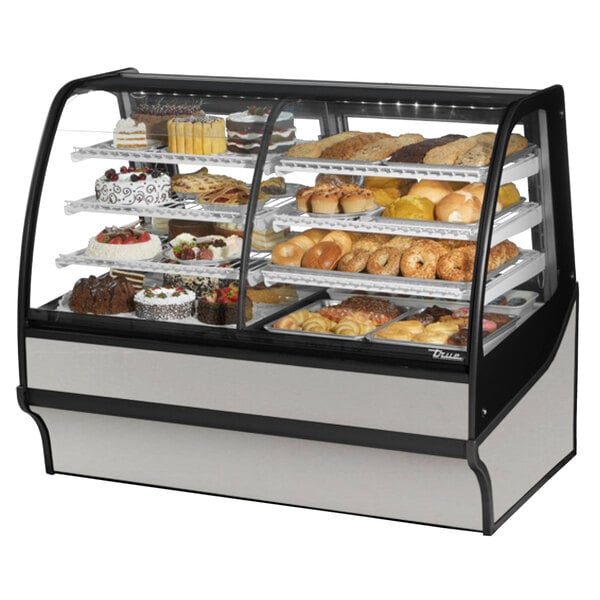 A True refrigerated bakery display case with curved glass and stainless steel interior on a counter with different types of pastries.