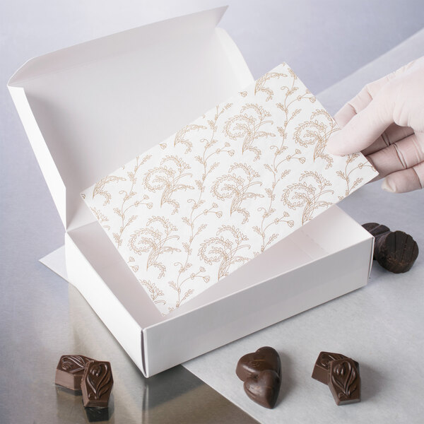 A hand placing a gold floral pad in a white candy box.