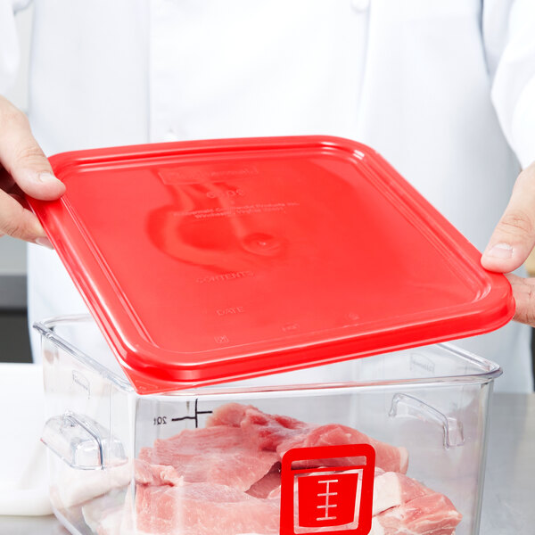 A chef using a red Rubbermaid food storage container lid to cover a container of meat.