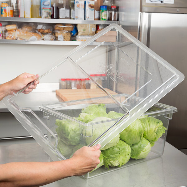 A person sliding a clear plastic lid onto a food storage box filled with lettuce.