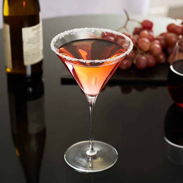 A Libbey Renaissance martini glass filled with pink liquid and garnished with grapes on a table.