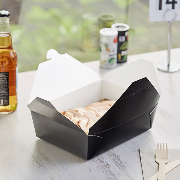 A black folded paper take-out box with food inside on a table.