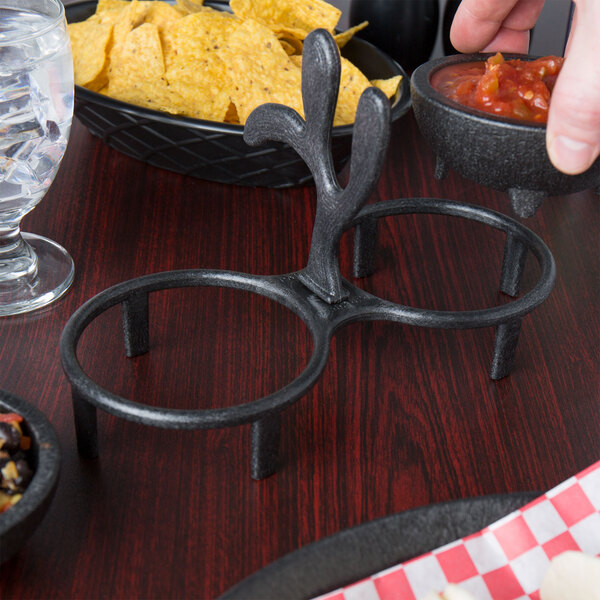A metal holder with two molcajetes of salsa in it on a table with a bowl of chips.