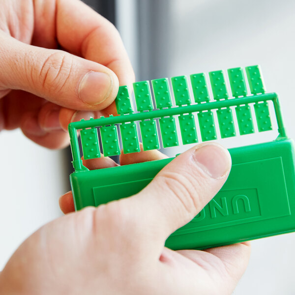 A hand holding a green plastic box with Unger PCLIP window cleaning plastic clips inside.