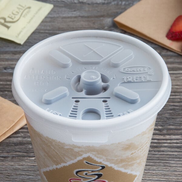 A white Dart foam cup with a translucent lift'n'lock lid and straw sitting on a table.