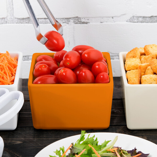 An orange Tablecraft straight sided bowl filled with tomatoes and croutons on a table in a salad bar.