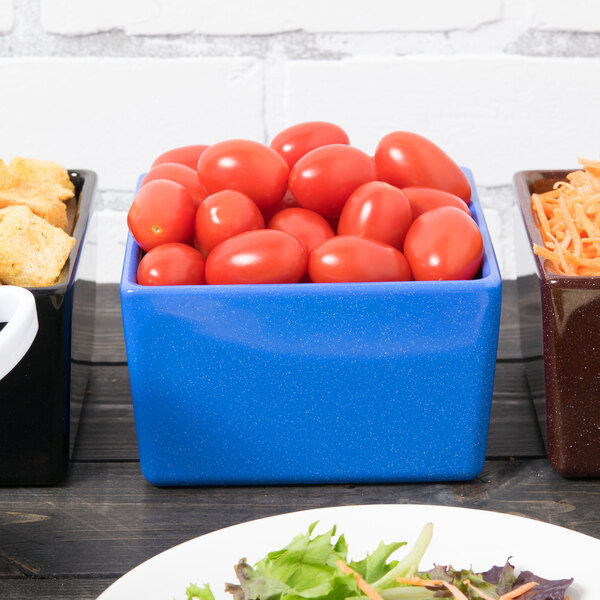 A blue Tablecraft square bowl with red tomatoes in it on a table.