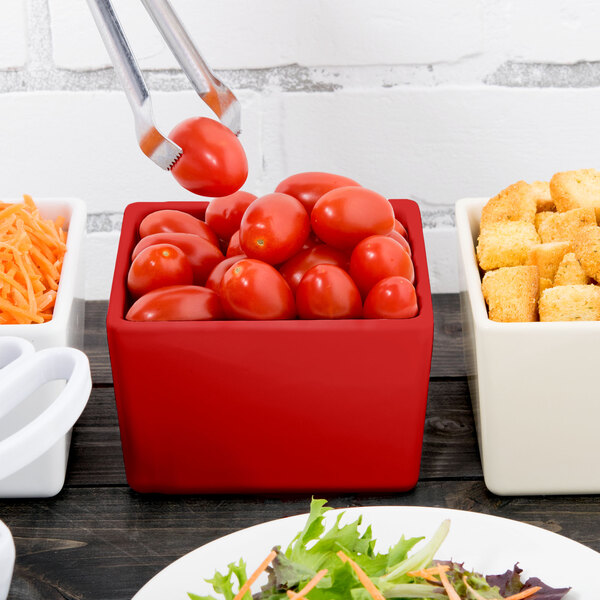 A red Tablecraft bowl filled with tomatoes on a table.