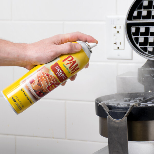 A person using PAM Saute & Grill Release Spray on a waffle iron.