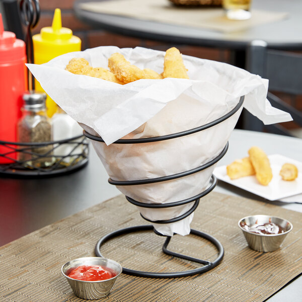 A black Clipper Mill spiral wire cone basket filled with chicken nuggets and a bowl of red sauce.
