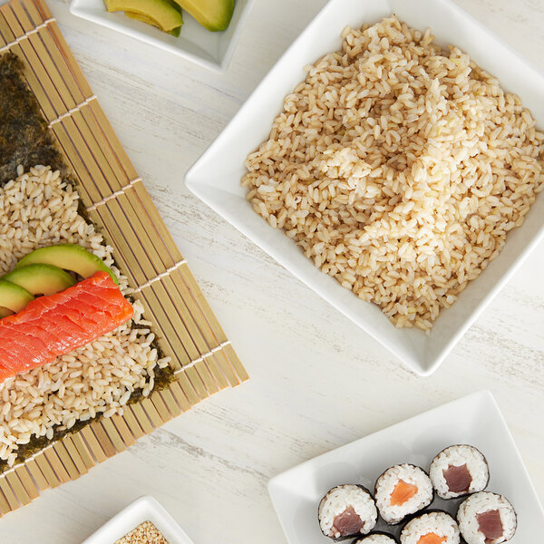 A white bowl of brown short grain rice on a table with sushi.