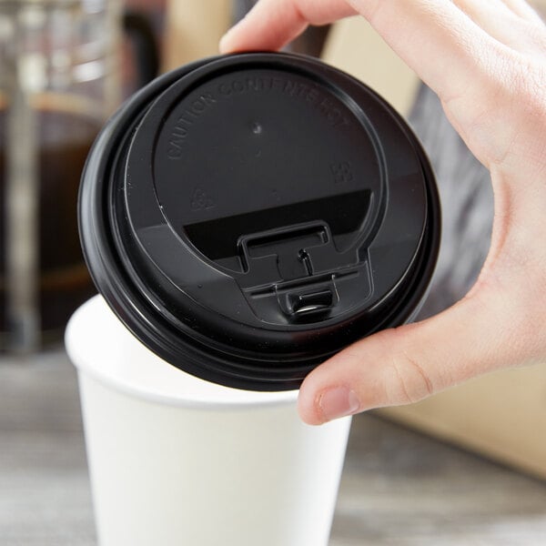 A hand holding a black Choice paper cup lid over a white cup of coffee.