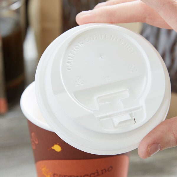 A person's hand using a white plastic travel lid on a coffee cup.