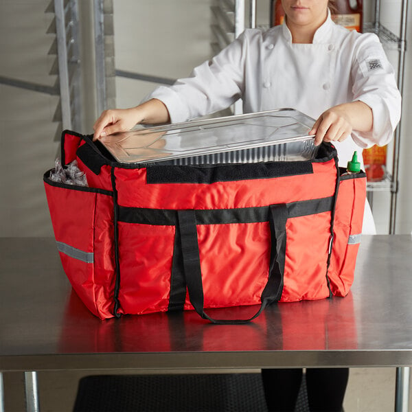 A woman in a chef's uniform holding a large red ServIt food delivery bag.