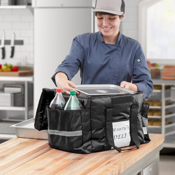 A woman in a chef hat using a ServIt insulated delivery bag to hold a tray and bottles.