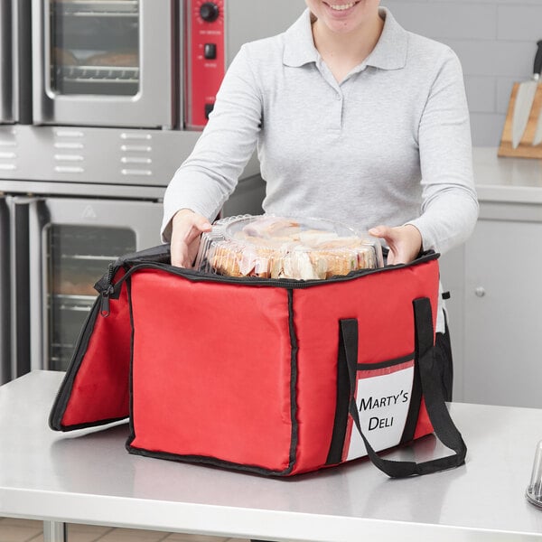 A woman holding a red Choice insulated delivery bag full of food.