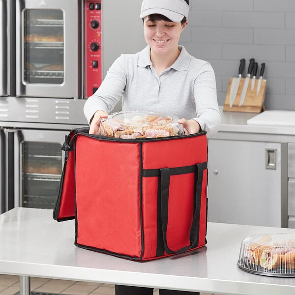 A woman in a white cap putting food in a red Choice insulated food delivery bag.