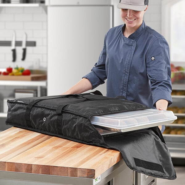 A woman in a chef hat holding a black ServIt bag on a metal tray in a professional kitchen.