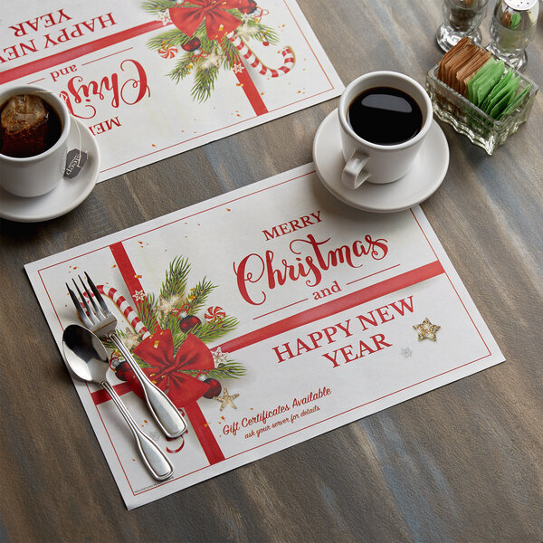 A Hoffmaster Holiday Ornaments placemat with a fork and spoon on it on a table with cups of coffee.