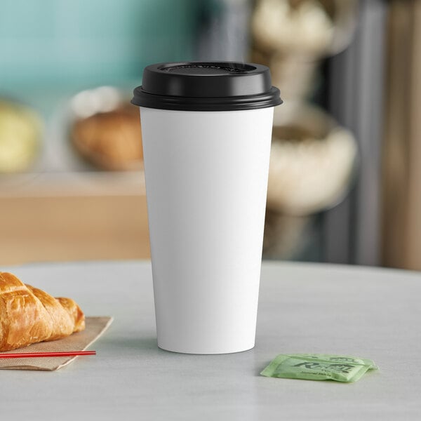 A white Choice paper hot cup with a black lid on a table with a croissant and bag.