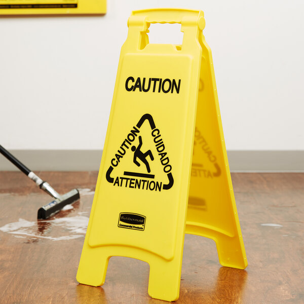 A yellow Rubbermaid caution sign on a wood floor.