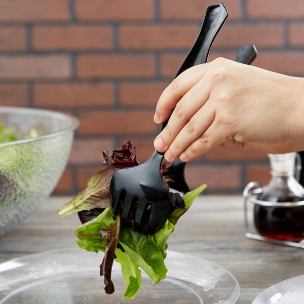 A hand holding a black Choice plastic serving fork over a salad