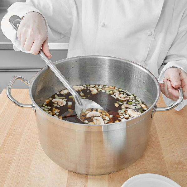 A person stirring a pot of soup with a Vollrath slotted basting spoon.
