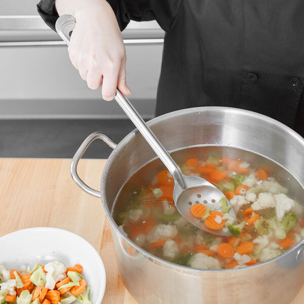 A person using a Vollrath perforated basting spoon to stir a pot of vegetables and meat.
