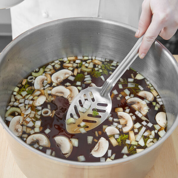A person using a Vollrath slotted basting spoon to stir soup in a pot.