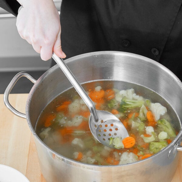 A person using a Vollrath perforated basting spoon to stir soup in a pot.