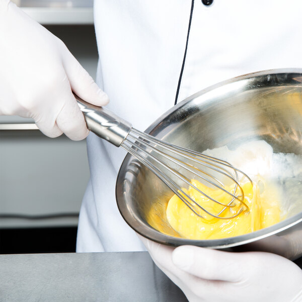 A person in white gloves using a Vollrath stainless steel whisk to mix eggs in a bowl.