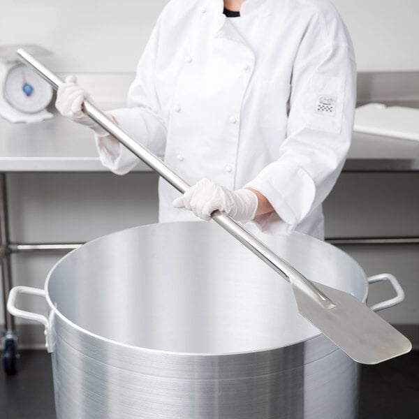 A person in a white chef's coat holding a large metal paddle.