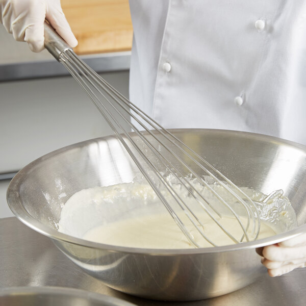 A person in a white coat using a Vollrath stainless steel French whisk to mix a bowl of white substance.