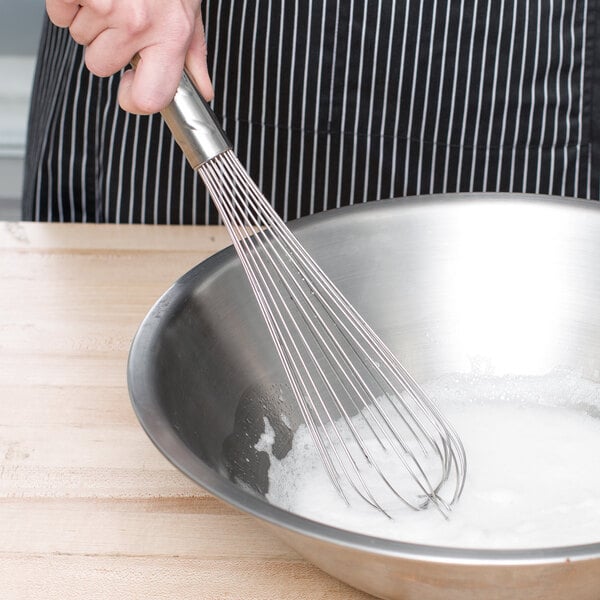 A person using a Vollrath stainless steel piano whisk to stir flour in a bowl.