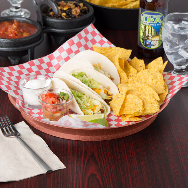 A round paprika deli server filled with tacos and a glass of salsa on a table in a Mexican restaurant.