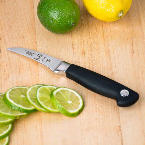 A Mercer Culinary Genesis forged bird's beak peeling knife next to sliced limes.