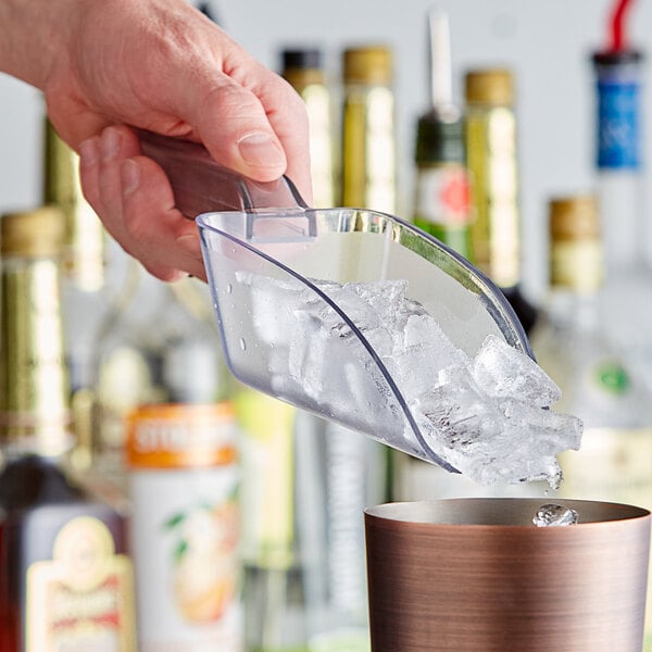 A person's hand using a Choice clear plastic utility scoop to add ice to a cup.