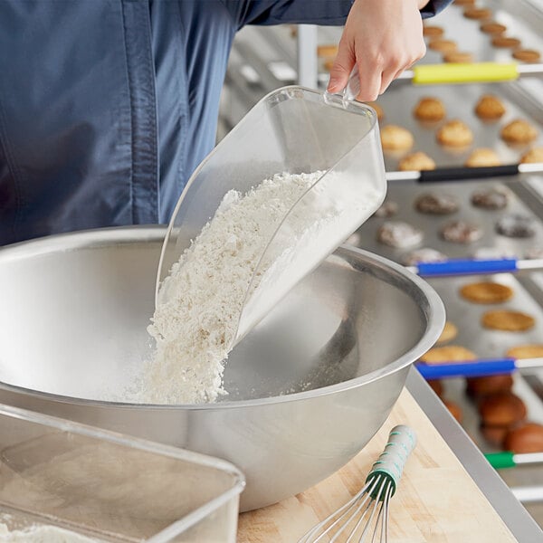 A person using a Choice clear plastic utility scoop to pour white flour into a bowl.
