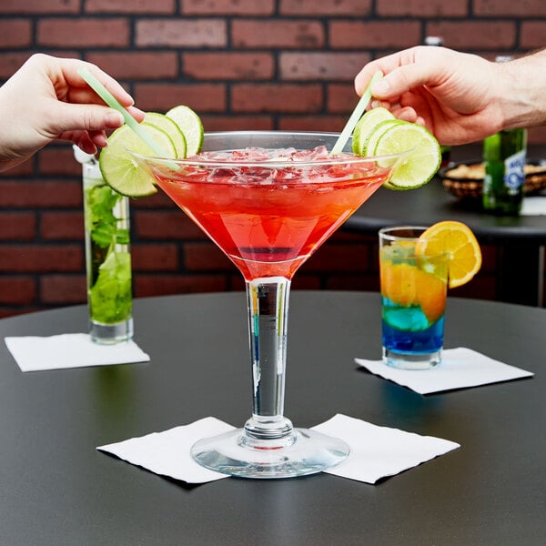 Two people holding Libbey Super Martini Glasses filled with red drinks and lime slices.