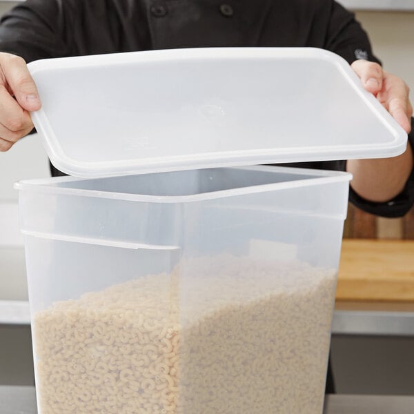A man holding a Carlisle translucent rectangular plastic food storage container with a lid open.