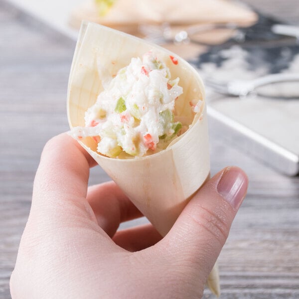 A hand holding a small wooden cone filled with food.