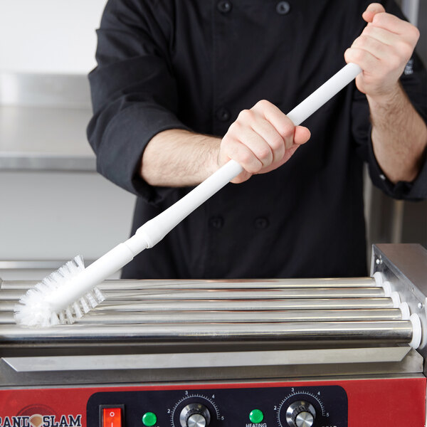 A person using a Carlisle Sparta Spectrum brush to clean a hot dog roller.