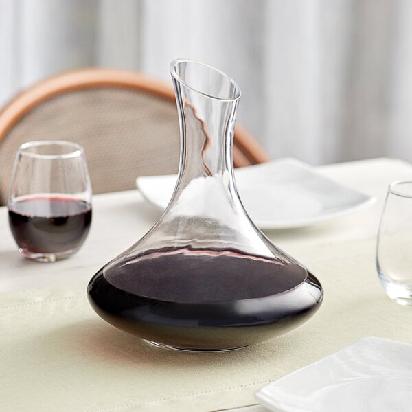 An Acopa glass wine decanter filled with red wine on a table.
